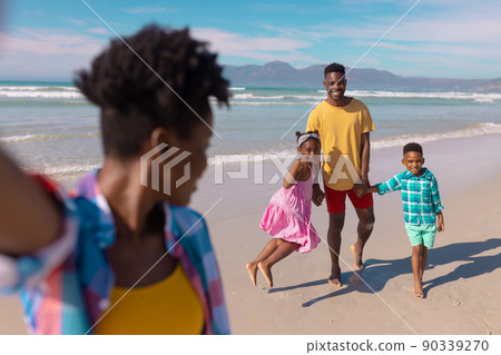 African american young woman looking at happy son, daughter and boyfriend at beach against sky 90339270