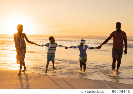 African american young parents holding son and daughter's hands while standing at shore against sky 90339448