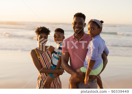 Portrait of smiling african american young parents carrying son and daughter against sea and sky 90339449