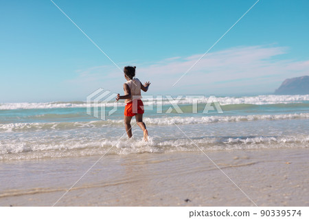 Rear view of playful african american girl running in sea against blue sky on sunny day 90339574