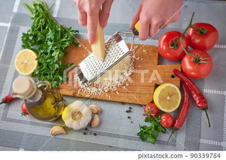 Woman grating parmesan cheese on a grater at domestic kitchen 90339784