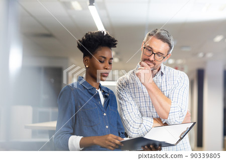 Confident biracial colleagues planning together while discussing over file at modern workplace Confident biracial colleagues planning together while discussing over file at modern workplace 90339805