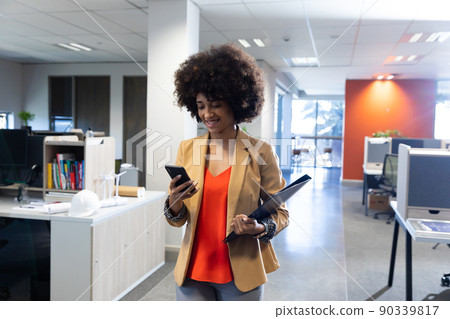 Smiling hispanic businesswoman walking while using smartphone at modern workplace Smiling hispanic businesswoman walking while using smartphone at modern workplace 90339817