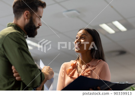 Happy biracial businesswoman discussing over document with caucasian businessman in workplace Happy biracial businesswoman discussing over document with caucasian businessman in workplace 90339913