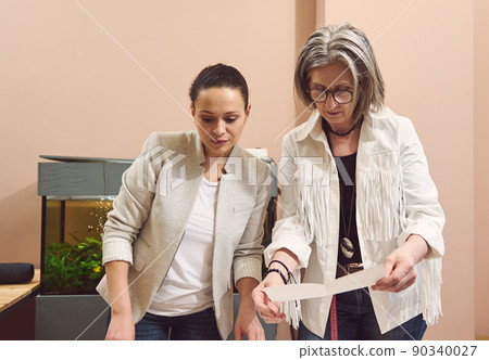 Two women of different nationalities and age working together on sewing pattern while creating new garment in a fashion design and tailoring atelier 90340027