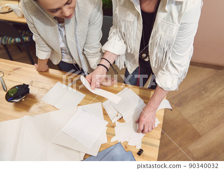 Overhead view of a skilled team of fashion designers working at a wooden table in clothing design studio and creating sewing patterns for new collection Overhead view of a skilled team of fashion designers working at a wooden table in clothing design studio and creating sewing patterns for new collection 90340032