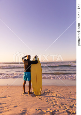 Rear view of african american senior man with surfboard looking at seascape against clear sky Rear view of african american senior man with surfboard looking at seascape against clear sky 90340168