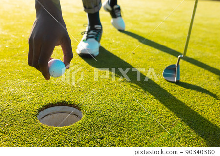 Cropped image of african american young man putting golf ball in hole at golf course in summer 90340380
