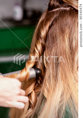 The female hairdresser is curling hair for a brown-haired young caucasian woman in a beauty salon The female hairdresser is curling hair for a brown-haired young caucasian woman in a beauty salon 90340474