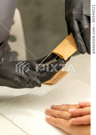 Manicure master takes out manicure tools from a kraft envelope in a nail salon Manicure master takes out manicure tools from a kraft envelope in a nail salon 90340521