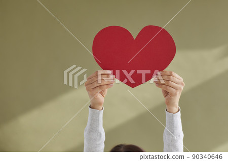 Woman holding up red mockup heart shaped valentine card against green background Woman holding up red mockup heart shaped valentine card against green background 90340646
