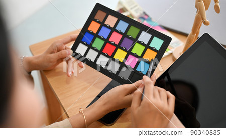 A colour checker board in a female graphic designer's hand over the office desk. A colour checker board in a female graphic designer's hand over the office desk. 90340885