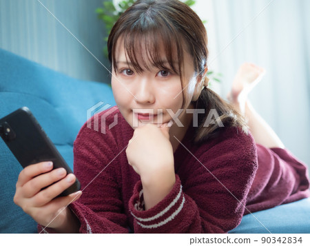 一個女人躺在沙發上操作智能手機 90342834