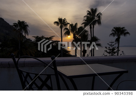 Sunset view through palm trees from balcony with table and chairs 90343398