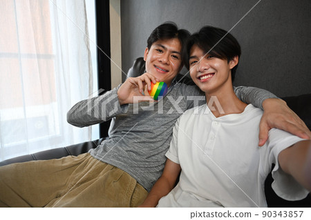 Young gay couple embracing and holding rainbow heart shape. LGBT, pride, relationships and equality concept 90343857