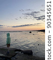Sea at sunset. A boy in a hoodie looks at the horizon 90345651