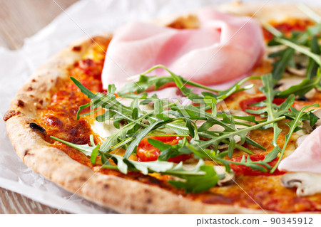 Hot italian pizza with prosciutto and arugula on a table. Hot italian pizza with prosciutto and arugula on a table. 90345912