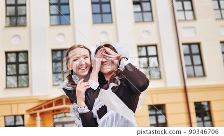 Happy schoolgirl graduate closes her friend's eyes. Happy schoolgirl graduate closes her friend's eyes. 90346706