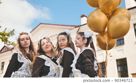 Cheerful Russian girls graduating with orange balloons on the last school day. Cheerful Russian girls graduating with orange balloons on the last school day. 90346721