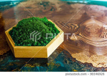 Stabilized moss in a hexagonal wooden box stands on an epoxy resin table. Eco-friendly interior detail, showcase for displaying items for sale Stabilized moss in a hexagonal wooden box stands on an epoxy resin table. Eco-friendly interior detail, showcase for displaying items for sale 90346926
