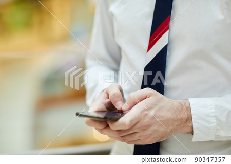 Close-up of unrecognizable bank employee in necktie and white shirt standing and making note in smartphone 90347357