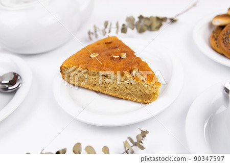 A piece of cake on a saucer with a cup for tea or coffee and a kettle 90347597