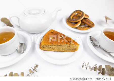 A piece of cake on a saucer with a cup for tea or coffee and a kettle A piece of cake on a saucer with a cup for tea or coffee and a kettle 90347601