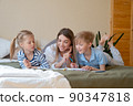 Mother and her two children drawing together at home laying on bed sofa 90347818