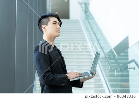 A young businessman standing in front of the stairs of an office building with a PC shooting cooperation "LINK FOREST" 90348336