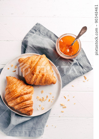 Plate with two fresh croissants and jam on white wooden table. Top view. 90348461