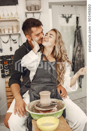 Mutual creative work. Young beautiful couple in casual clothes and aprons. People creating a bowl on a pottery wheel in a clay studio. 90349860