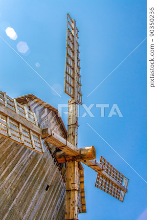Old windmill. View of wooden wings of windmill from below against the blue sky. Close-up. Vertical photo Old windmill. View of wooden wings of windmill from below against the blue sky. Close-up. Vertical photo 90350236