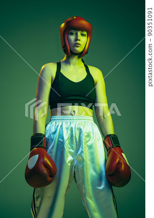 Professional female boxer in sports protective equipment posing isolated on cyan color studio background in neon. Sport, competition, hobby, results, success concept 90351091
