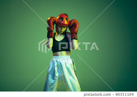 Cropped portrait of professional female boxer in sports protective equipment posing isolated on cyan color background in neon filter. Sport, competition, hobby, results, success concept 90351104