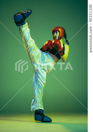 Professional female boxer in boxing gloves and helmet in action, motion isolated on green studio background in neon light. Sport, competition, challenges, results, success concept Professional female boxer in boxing gloves and helmet in action, motion isolated on green studio background in neon light. Sport, competition, challenges, results, success concept 90351106