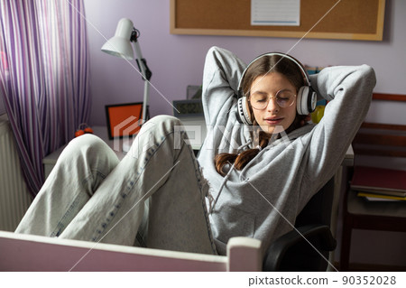A teenager relaxes by listening to music on wireless headphones. A teenager relaxes by listening to music on wireless headphones. 90352028
