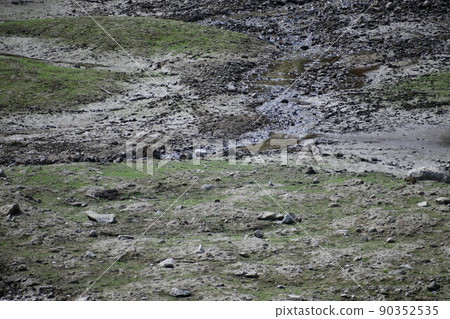 A view of the bottom of a pond with a little damp water and no water A view of the bottom of a pond with a little damp water and no water 90352535