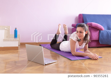 Happy young caucasian woman watching exercise classes on her laptop in her living room. Health care and wellness at home concept. Happy young caucasian woman watching exercise classes on her laptop in her living room. Health care and wellness at home concept. 90355261