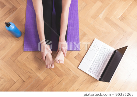 Young happy caucasian woman stretching in the living room while looking at her laptop. Health care and wellness at home concept. Young happy caucasian woman stretching in the living room while looking at her laptop. Health care and wellness at home concept. 90355263