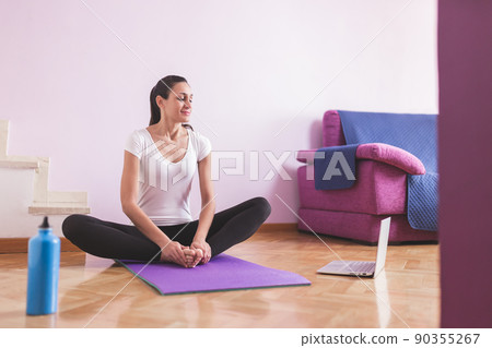 Young happy caucasian woman stretching in the living room while looking at her laptop. Health care and wellness at home concept. Young happy caucasian woman stretching in the living room while looking at her laptop. Health care and wellness at home concept. 90355267