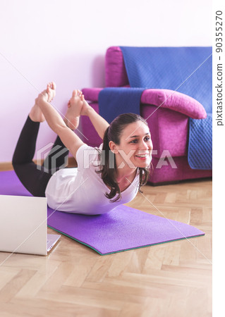 Young happy caucasian woman stretching in the living room while looking at her laptop. Health care and wellness at home concept. Young happy caucasian woman stretching in the living room while looking at her laptop. Health care and wellness at home concept. 90355270