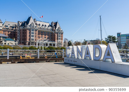 Victoria, BC, Canada - April 14 2021 : Canada Sign, Victoria Inner Harbour. Historical buildings in the background over blue sky. Hotel Fairmont Empress. 90355699