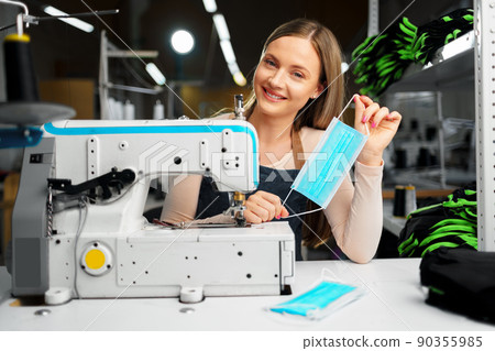 Smiling young blonde seamstress putting on medical protective mask 90355985
