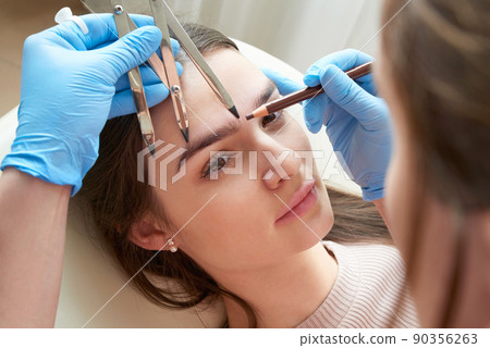 Cosmetologist measures the proportions of the eyebrows with the ruler. Cosmetologist measures the proportions of the eyebrows with the ruler. 90356263