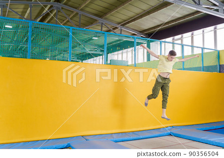 Teenage boy jumping on trampoline park in sport center  90356504