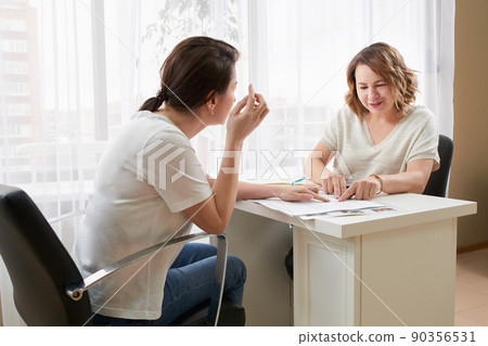 Young woman studying with private tutor at a table taking notes and reading Young woman studying with private tutor at a table taking notes and reading 90356531