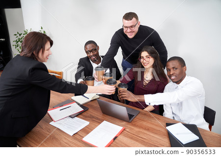 Young happy business people working together in modern office, multiethnic teamwork. Toasting with coffee cups Young happy business people working together in modern office, multiethnic teamwork. Toasting with coffee cups 90356533