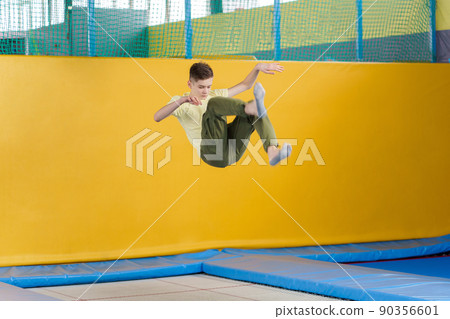 Teenage boy jumping on trampoline park in sport center Teenage boy jumping on trampoline park in sport center 90356601