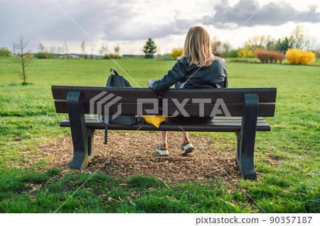 Happy blonde woman in style clothes resting, relaxing sitting on bench and enjoying in city green nature park outdoors. Back view  90357187