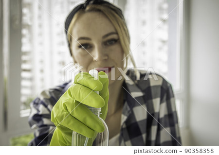Pretty woman sprays window cleaner on glass. Pretty woman sprays window cleaner on glass. 90358358